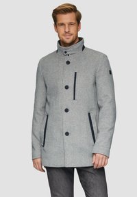 Grijze wolmix jas met hoge kraag, zwarte knopen, twee zijzakken en marineblauwe accenten op de borst, getoond op een model tegen een lichte achtergrond.