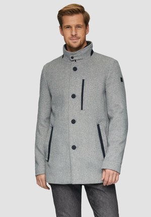 Manteau en mélange de laine gris avec un col montant, boutons noirs, deux poches latérales et accents bleu marine sur la poitrine, présenté par un modèle sur un fond clair.