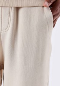 Beige joggingbroek gemaakt van een zachte stof, met een geribbelde tailleband, zijzakken en zichtbare stiksels.