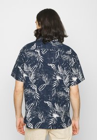 Short-sleeve shirt in navy blue with white tropical leaf print, featuring a collar and a relaxed fit. Textured fabric with a casual design.