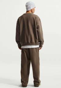 Sweat-shirt marron et pantalon assorti en tissu doux, avec une coupe décontractée. Un bonnet blanc ajoute du contraste. Détails de couture visibles sur les bords.