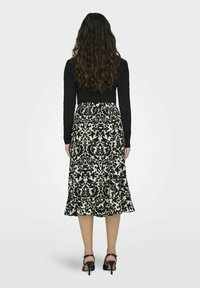 Musta pitkähiha toppi yhdistettyinä puolipitkään hameeseen, jossa on musta-valkoinen kukkakuosi, röyhelöhelma ja mustat narukenkiä.