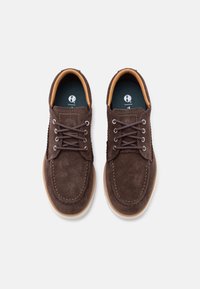 Καφέ σουέτ παπούτσια με κορδόνια, στρογγυλεμένες μύτες και μπεζ λαστιχένιες σόλες. Διαθέτουν ραφές ίδιου χρώματος και αντίθετη εσωτερική επένδυση.