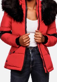 Rød pufferjakke med hætte af sort pels, med lynlåslukning, elastiske forsyninger og sidelommer. Bæres over en hvid top og mørke jeans.