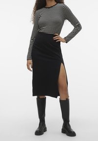 Czarna midi spódnica z bocznym rozcięciem w połączeniu z czarno-białą pasiastą bluzką z długim rękawem. Modelka ma na sobie czarne kozaki za kolano. Gładka struktura materiału.