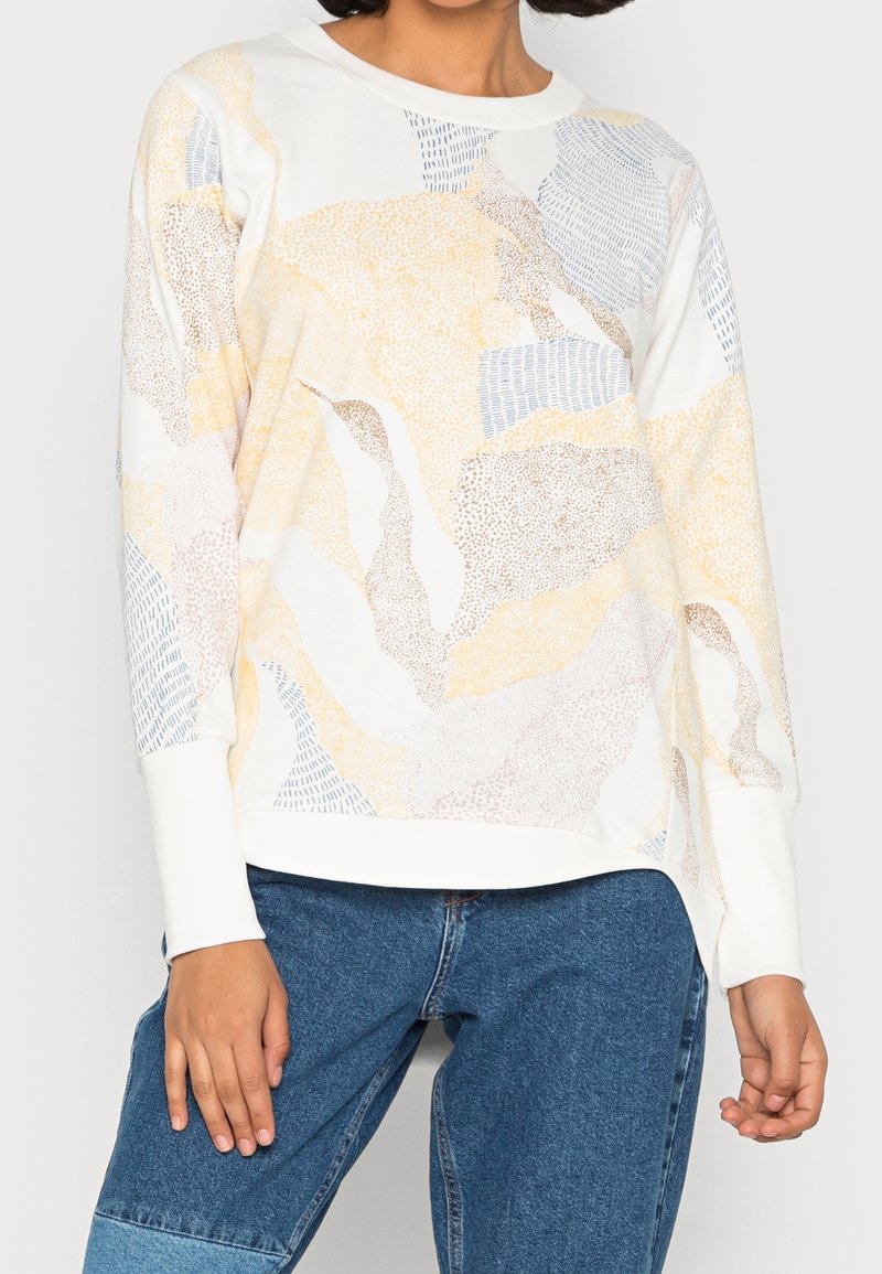 Sudadera blanca con patrones abstractos en amarillo, marrón y azul. Presenta mangas largas y puños acanalados. Tela suave y corte relajado.