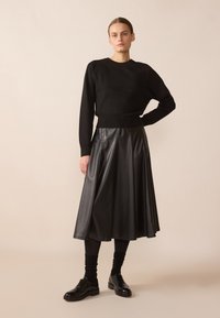 Svart stickad tröja med en figursydd midja, kombinerad med en flödande svart läderkjol. Accessoarer inkluderar svarta snörskor och mörka strumpor.
