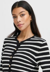 Cardigan rayé noir et blanc avec un col rond et des boutons dorés, présentant un design en tricot texturé.