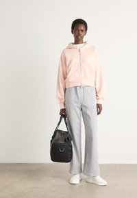 Felpa cropped color rosa chiaro con zip frontale, abbinata a pantaloni in felpa grigi a gamba larga. Borsa nera con un dettaglio in metallo argentato. Sneakers bianche.