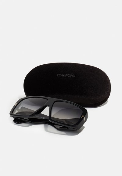 Sort Tom Ford solbriller med en tyk ramme, grå gradientlinser og en gylden accent. Inkluderer et sort, blødt etui.