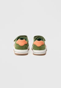 Grønne semskede sko med oransje aksent på hælen, hvit mellomsåle og teksturert brun gummisåle. Borrelåsrem på toppen for lukking.