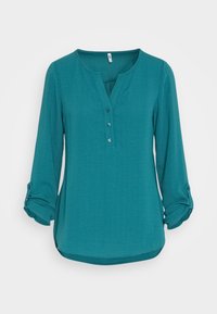 Chemise à manches longues couleur sarcelle avec un col en V et trois boutons sur le devant. Dispose de manches retroussables fixées par des boutons et d'un ourlet arrondi.