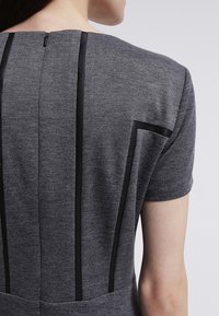 Grå klänning med en texturerad stickad tyg, korta ärmar och svarta accentpaneler längs ryggen och sidorna, samt en dold dragkedja.