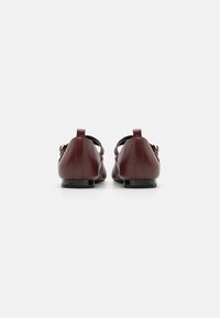 Chaussures plates en cuir bordeaux avec un bout arrondi, un petit talon et un détail de bride ajustable à la cheville. Texture lisse avec un matériel minimal.