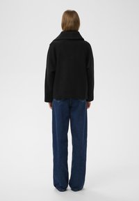 Sort uldjakke med bred krave, parret med løstsiddende mørkeblå denim jeans. Enkel design, ingen synlige mønstre eller accenter.