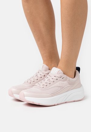 Zapatillas deportivas de color rosa claro con material de malla y sintético, con una suela blanca, costuras prominentes y un logo en la lengüeta.