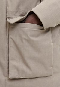 Bežna oblačila z gladko teksturo, velikim sprednjim žepom in sproščenim krojem. Tkanina se zdi lahka in udobna.