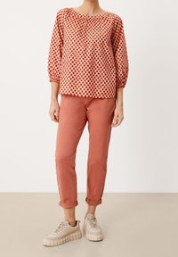 Rød- og hvidmønstret langærmet top med samlet halsudskæring, parret med peachfarvede bukser med opprullede ærmer og beige klodsede sneakers.