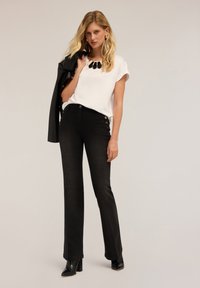 Vaqueros negros acampanados con acentos de botones, combinados con una blusa blanca de manga corta y una chaqueta de cuero negra. Tejido suave y diseño estructurado.