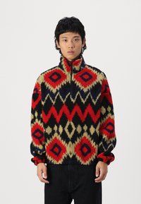 Fleece pullover features a multicolored geometric pattern with red, black, and beige. High collar and elasticized cuffs. Soft texture.