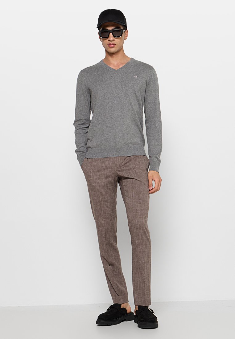 Grau V-Ausschnitt-Pullover, braune Karohose, schwarze Sonnenbrille und schwarze Kappe. Slim Fit; weiche Textur mit gerippten Bündchen und Taillenbund.