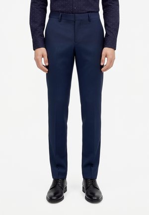Mannequin portant un pantalon de costume bleu marine, une chemise bleue à pois et des chaussures noires à lacets sur fond blanc.