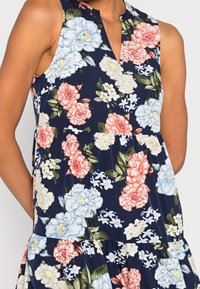 Blommönstrad ärmlös klänning i marinblått tyg, med rosa, vita och blå blommor, V-ringning och rynkad midjedetalj.