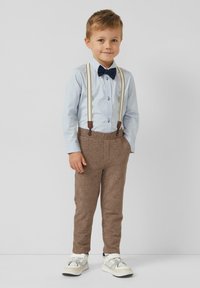 Jasnoniebieska koszula na guziki, granatowa mucha, brązowe spodnie o fakturze z szelkami oraz białe trampki z czarnymi dodatkami.