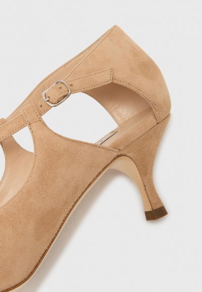 Beige zamšas augstpapēžu kurpe ar izgriezumu, regulējama potītes siksniņa ar sudraba sprādzi un elegants, sašaurināts papēdis.