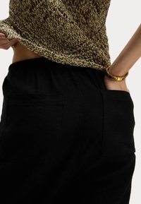 Pantaloni neri larghi realizzati in un tessuto morbido con due tasche posteriori. La parte superiore presenta un design a maglia dorata testurizzata, parzialmente infilata dentro. 