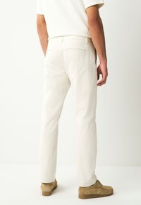 Pantaloni beige chiaro a taglio dritto, con vita standard, tasche posteriori e una texture liscia in cotone. Abbinati a scarpe in suede marrone.