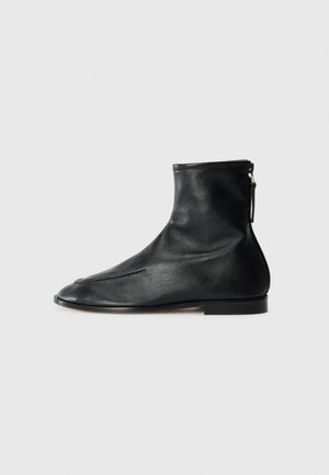 Botas de tobillo de cuero negro con diseño de punta afilada, textura suave y cremallera lateral para facilitar su uso. Tacón bajo, estilo minimalista.