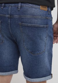 Denimshorts i mörkblått med uppvikt kant. Har två bakfickor och en läderlogotyp på midjebandet.