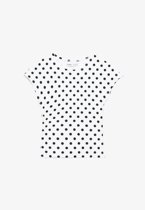 Camicia bianca a maniche corte con pois neri, scollo rotondo e linea leggermente aderente, distesa su uno sfondo bianco.