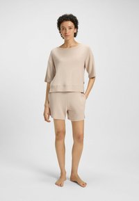 Beige loungewear set met een losse, vierkante top met brede mouwen en bijpassende shorts. De stof heeft een subtiele textuur en een zachte afwerking.