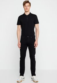 Polo shirt nera a maniche corte, con colletto e quattro bottoni. Abbinata a jeans neri slim-fit e sneakers bianche con accenti verdi.