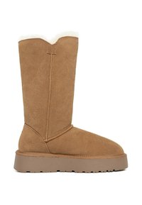 Botas de ante marrón hasta la rodilla con puntera redondeada, suela de goma gruesa y suave borde de piel blanca en la parte superior, con detalles de costura visibles.