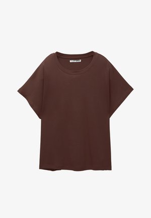 Hnědý oversized tričko vyrobené z bavlny, s kulatým výstřihem, krátkým rukávem a uvolněným střihem. Hladký povrch bez viditelných vzorů.