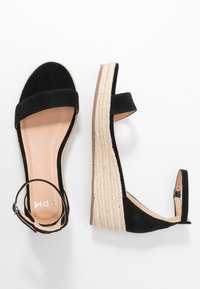 Black suede wedge sandals with an ankle strap, featuring a braided jute platform and smooth leather insole. Minimalist design with dual straps.