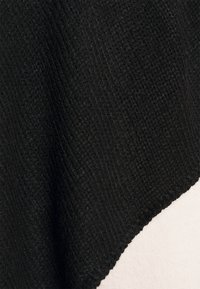 Μαύρος υφασμάτινος ιστός υπό γωνία, με μια λεία λευκή περιοχή από κάτω. Ο μαύρος ιστός έχει πλεκτό σχέδιο, υποδηλώνοντας μια μαλακή υφή.