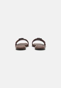 Sandalias de cuero marrón con dos correas curvadas y una suela plana. Detalle de textura sutil en la plantilla, diseño minimalista, sin herrajes visibles.