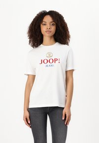 Baltos medvilninės marškinėliai su raudonu „JOOP!“ ir mėlynu „JEANS“, viršuje su apvaliu logotipu. Trumpomis rankovėmis ir laisvu siluetu.