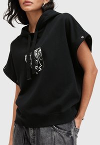 Černá zkrácená mikina s kapucí vyrobená z měkké tkaniny, která má grafický design na přední straně, nastavitelné šňůrky a knoflíkové detaily na rukávech.
