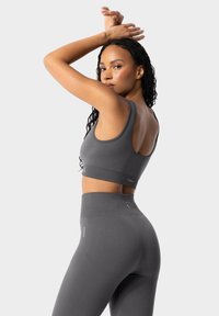 Sujeción deportiva gris y leggings de cintura alta hechos de un material suave y elástico. Presentan tirantes anchos y un sutil logotipo en la cinturilla.