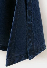 Tissu en denim bleu foncé montrant un gros plan de coutures soigneusement cousues et un tissage texturé.