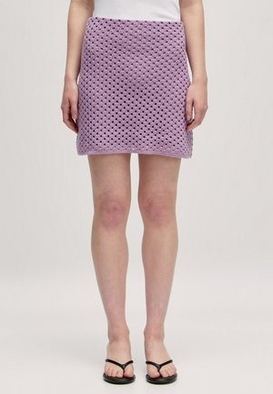 Lila gewebter Minirock mit einem strukturierten, offenen Strickdesign, geradem Schnitt und einem bequemen Bund. Kombiniert mit schwarzen Flip-Flops.