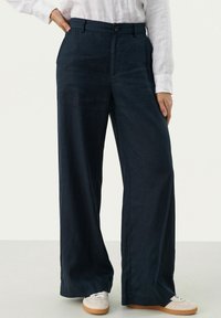 Marineblauwe wijde broek van lichtgewicht stof, met een knoopsluiting en zijzakken, gecombineerd met witte sneakers.
