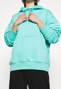 Mintgroene hoodie met een capuchon met trekkoord, kangoeroezak, geribbelde manchetten en een ontspannen pasvorm, gecombineerd met zwarte broek.