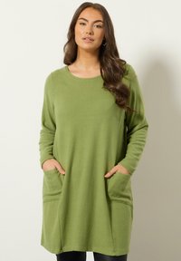 Groene tuniek met lange mouwen gemaakt van zachte stof, met een ronde halslijn en twee voorzakken. Losse pasvorm met een rechte zoom.
