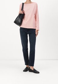 Top de manga larga rosa claro con rayas sutiles, combinado con jeans oscuros y zapatos negros tipo slip-on. Se sostiene un pequeño bolso de hombro de cuero negro.